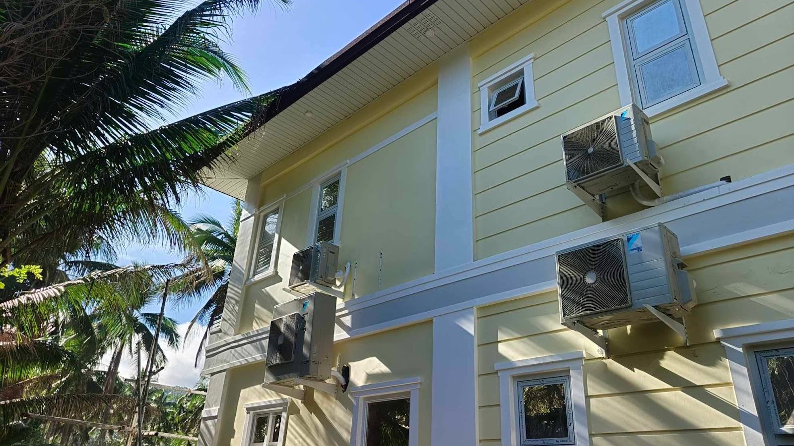 Two-storey coastal house with condensers mounted on the side facade, palms and blue sky