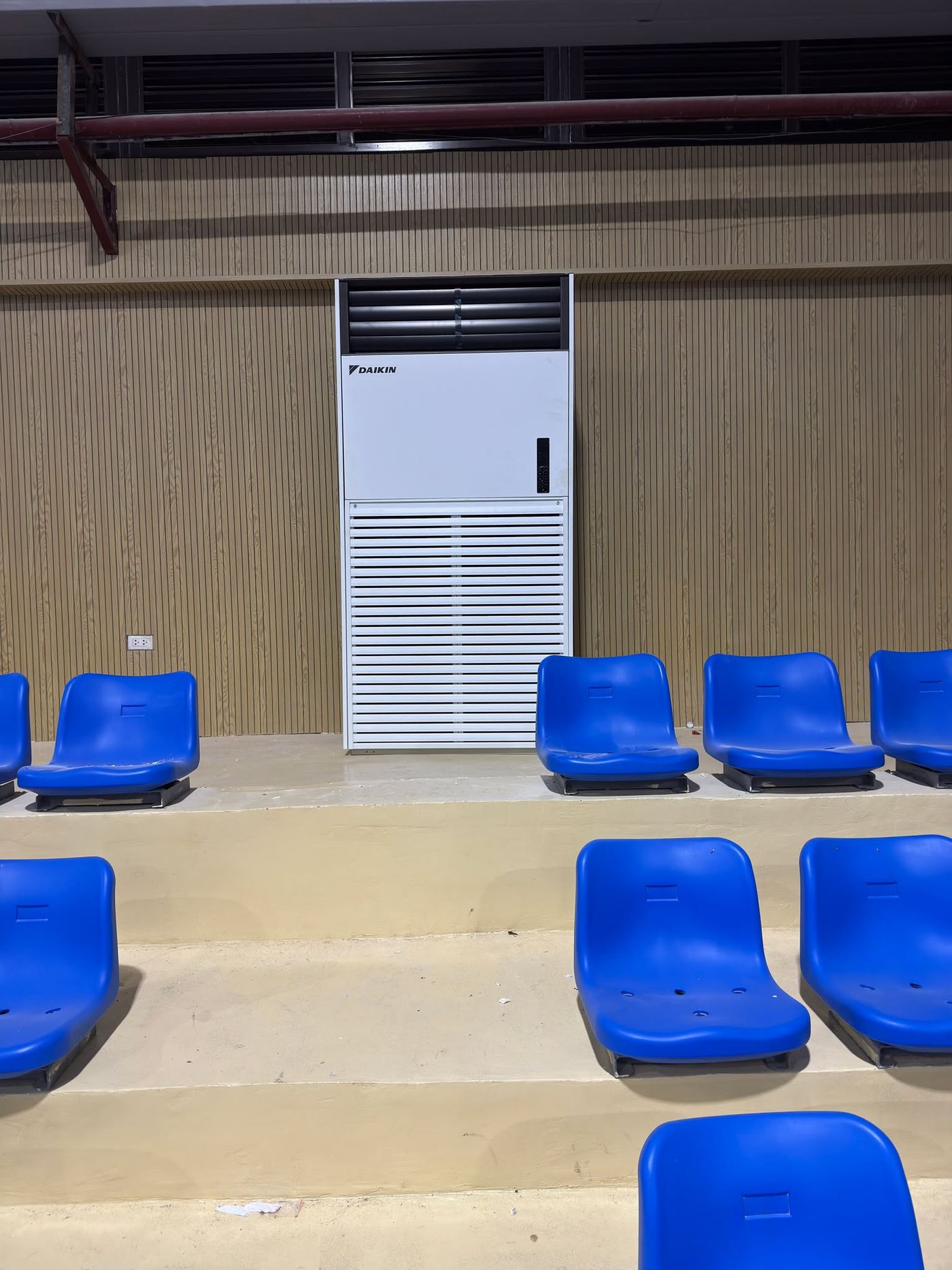 Auditorium with a large Daikin floor-standing unit beside tiered blue seating